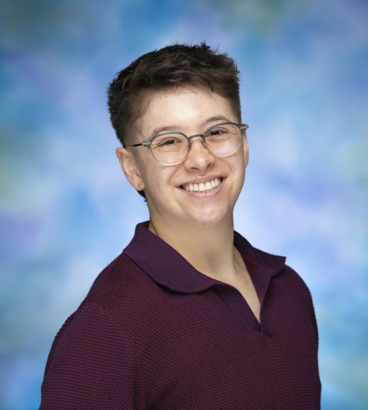 Megan smiles for a studio portrait with short hair, glasses, and a maroon shirt collared shirt.