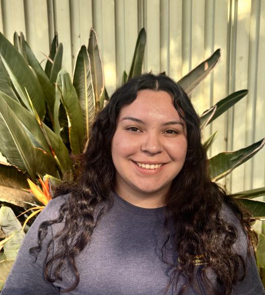 Young woman with long dark hair smiling in front of large agave plants